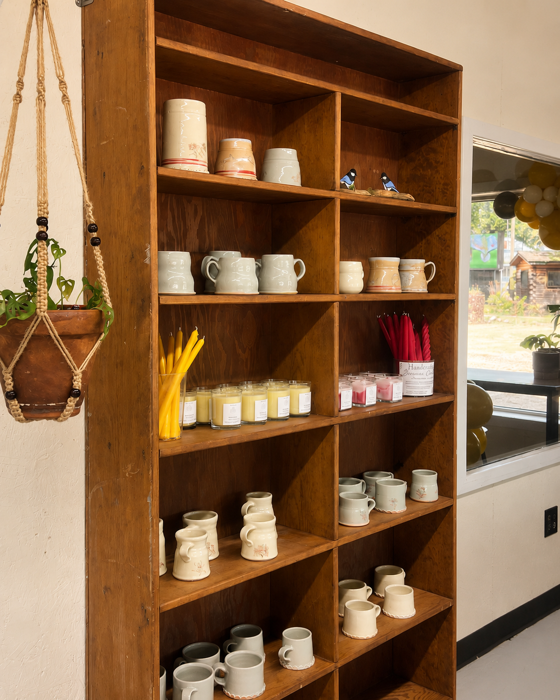 Tall wooden shelving filled with handmade mugs, vases, and candles