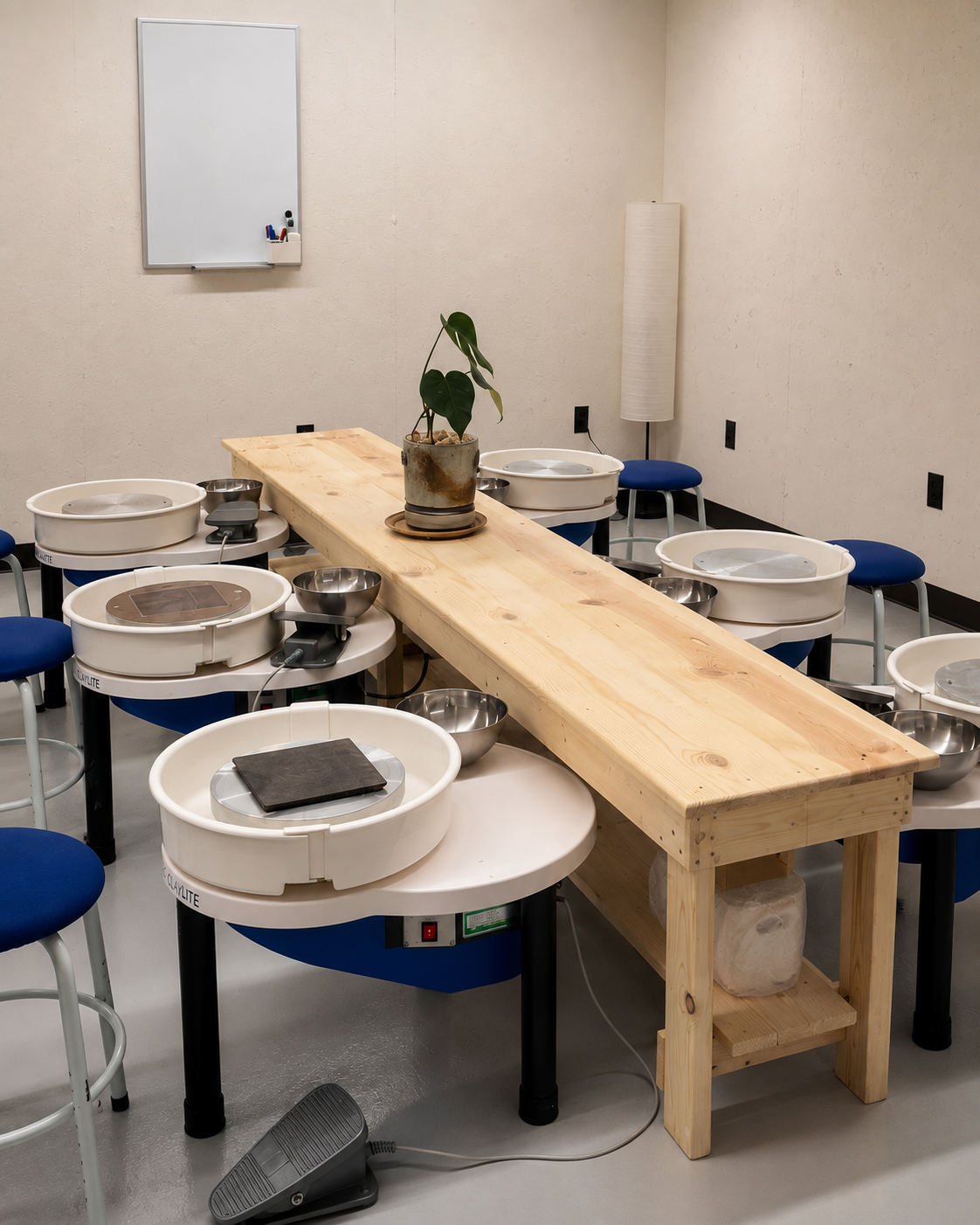 Pottery wheels lined up along a wooden worktable in the Village Pottery Studio classroom