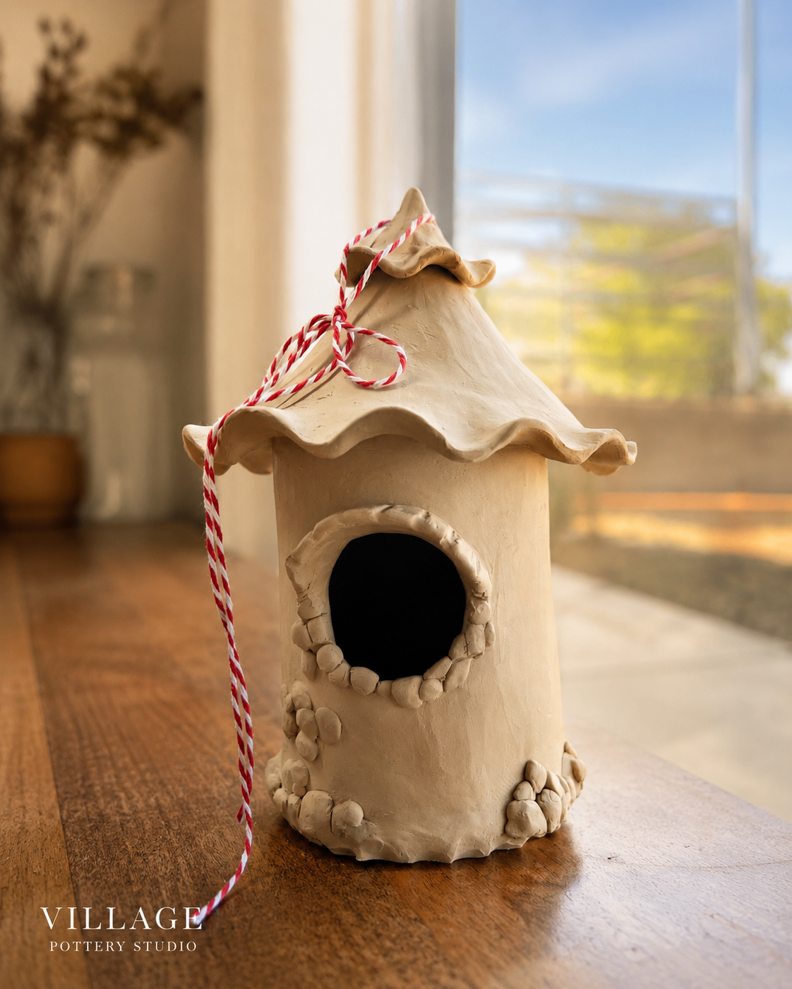Handmade ceramic birdhouse with a ruffled roof and red-and-white twine, made at Village Pottery Studio